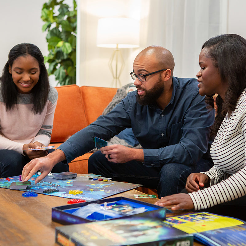 Load image into Gallery viewer, Pandemic Board Game lifestyle image of three people playing game with game box, rule book, and game contents displayed.