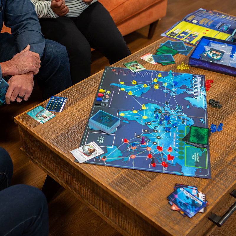 Load image into Gallery viewer, Pandemic Board Game lifestyle image of three people playing game with game box, rule book, and game contents displayed.