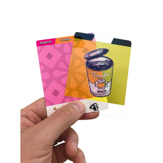 Pop Art Card Game - View of person holding a 'Magenta/orange' card and a yellow translucent tomato soup card. 